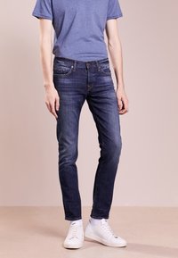 Mörkblå jeans i slim fit med klassisk femfickdesign, tillsammans med en kortärmad blå t-shirt och vita sneakers.