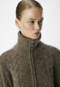 Suéter marrón de cuello alto con un collar acanalado, cierre de cremallera, material texturizado y un sutil patrón en forma de chevrón en el frontal.