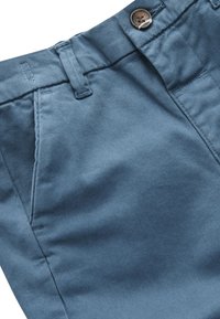 Pantaloni di cotone blu che mostrano la cintura con chiusura a bottone, passanti per la cintura e dettagli di cucitura delle tasche anteriori.