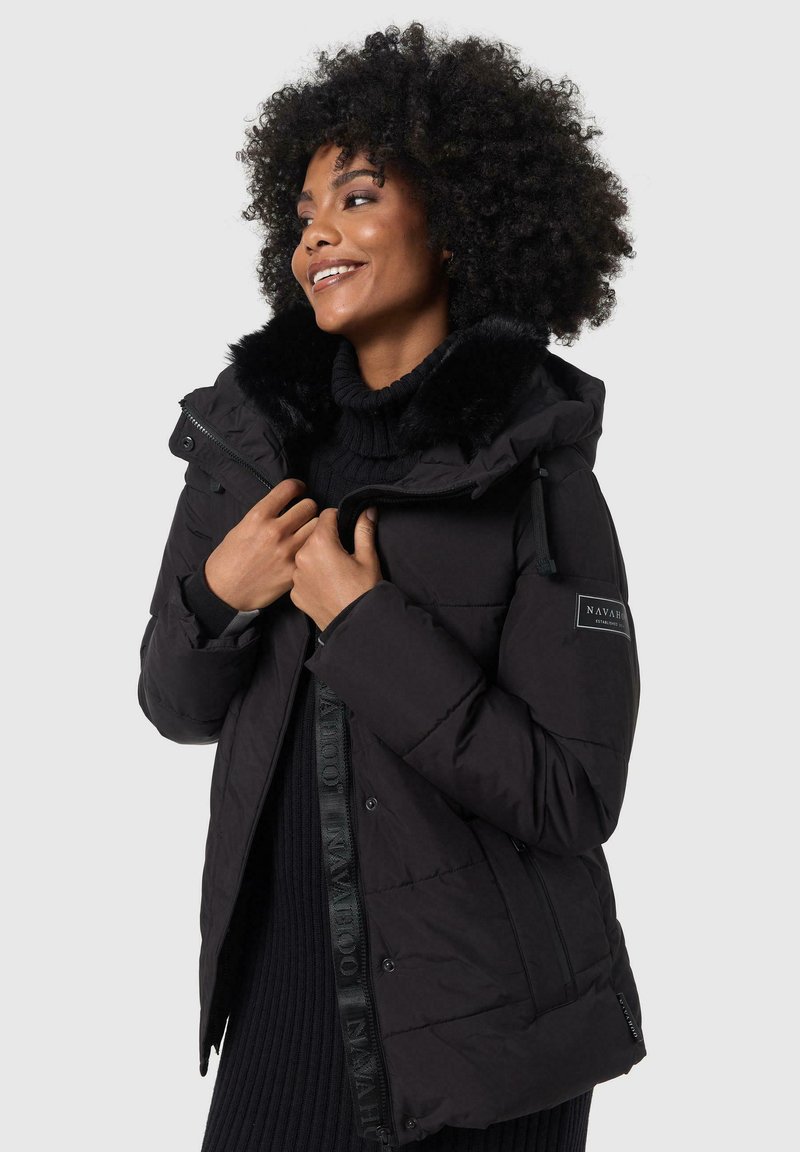 Black puffer jacket with a faux fur hood. Features a zip closure, quilted texture, and logo detailing on the side. Soft interior finish.