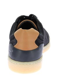 Zapatilla deportiva de ante negro con detalles en cuero tostado, parte trasera redondeada y suela de goma blanca; presenta una textura suave y talón reforzado.