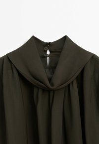 Robe vert olive foncé avec un large col plié et deux fermetures à boutons au niveau de l'encolure arrière.