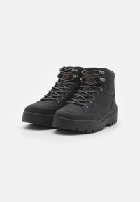 Stivali da escursionismo neri in suede con suole in gomma. Presentano lacci grigi, occhielli in metallo e dettagli del logo sui lati. Design a metà altezza.