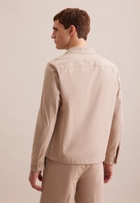 Camicia beige a maniche lunghe con taglio dritto, caratterizzata da un colletto classico e polsini con bottone, realizzata in un tessuto morbido, design semplice.