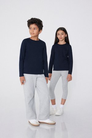 Des hauts à manches longues bleu marine, un pantalon de survêtement gris et des leggings sur deux enfants debout ; design simple avec un tissu doux et des couleurs neutres.