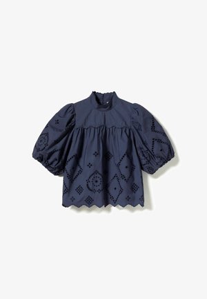 Tumesinine puuvillane pluus paistetavate varrukatega, kõrge kaelusega ja lainelise äärega. Omab keerukaid geomeetrilistes mustrites lõigatud tikandeid.