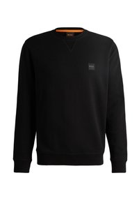 Sudadera negra hecha de tela suave, con cuello redondo, mangas largas, puños acanalados y un pequeño parche con logo negro en el pecho.