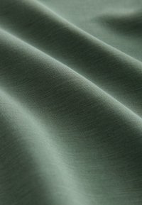 Green cotton fabric with a smooth texture, displaying subtle waves and folds. The material is lightweight and finely woven.