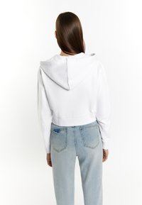 Witte crop hoodie met een zachte textuur en een capuchon, gecombineerd met lichtblauwe, high-waisted denim jeans met een versleten achterzak.