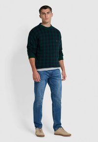 Groen geruit trui met ribbelkraag en -manchetten, gedragen over een grijs shirt, gecombineerd met blauwe spijkerbroeken en beige sneakers.