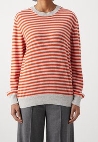 Maglione a righe arancione e grigio, con un collo rotondo, polsini e orlo a coste, dal tocco morbido. Abbinato a pantaloni grigi.