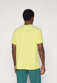 Αθλητική κοντομάνικη μπλούζα σε έντονο κίτρινο ύφασμα· διαθέτει υφασμάτινο πίσω πάνελ με υφή και στρογγυλή λαιμόκοψη. Λείου υφής, κανονική εφαρμογή.