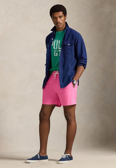 Μπλε πουκάμισο με κουμπιά πάνω από πράσινη φανέλα με γραφικά, ροζ σορτς και μπλε αθλητικά παπούτσια. Σημαντικές λεπτομέρειες: λογότυπο στα σορτς, άνετη εφαρμογή και χρώματα.