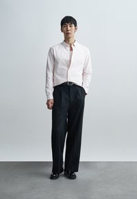 Ανοιχτό ροζ πουκάμισο με κάθετες ρίγες και μακριά μανίκια, συνδυασμένο με μαύρο, ψηλόμεσο παντελόνι και μαύρα δερμάτινα παπούτσια. Σχεδίαση στενής εφαρμογής, με κουμπιά.