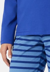 Blaues Langarmhemd kombiniert mit hellblauen Hosen, die dunkelblaue horizontale Streifen aufweisen. Der Stoff wirkt weich und hat eine lockere Passform.