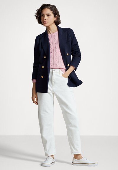 Blazer croisé bleu marine, pull en maille torsadée rose, pantalon blanc taille haute et baskets blanches avec des accents jaunes. Textures douces.