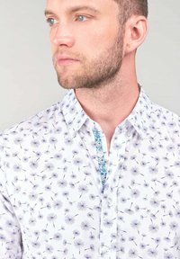 Witte blouse met paarse paardenbloemprints, lichtblauwe patroonaccenten langs de knopenlijst, klassieke kraag en regular fit.