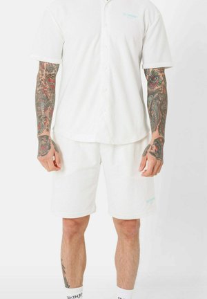 Chemise blanche à manches courtes, à boutons, avec un motif texturé, assortie à un short blanc. Comprend un détail de logo bleu clair.