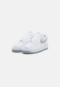 Hvide Nike Air Force 1 sko med en glat læderøvre, grå swoosh, perforeret tå og en tekstureret grå gummi sål.
