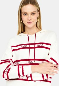 Felpa bianca con strisce orizzontali rosse, con testo "LIUJO". Cappuccio con cordino, fit rilassato e polsini a coste. Tessuto morbido.