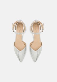 Chaussures argentées à bout pointu avec un design élégant, dotées d'une fine sangle à la cheville et d'une texture métallique lisse. La semelle intérieure est beige.