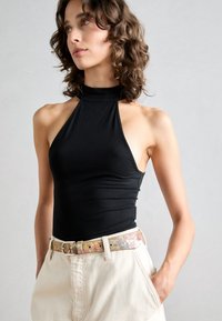 Black sleeveless halter top with a fitted design, paired with light-colored high-waisted trousers and a patterned floral belt.