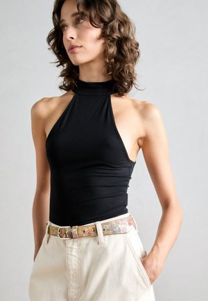 Top halter nera senza maniche con un design aderente, abbinato a pantaloni chiari a vita alta e una cintura floreale a fantasia.