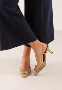 Zapatos slingback en tono dorado con punta afilada, diseño de tejido texturizado y lazo decorativo en el empeine; altura del tacón de 5 cm.