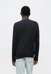 Pull en tricot côtelé bleu marine avec manches longues et col rond, présentant une surface texturée et une coupe légèrement décontractée.