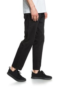 Zwarte, recht gesneden broek van duurzaam materiaal met zijzakken. Gecombineerd met zwarte, gestructureerde sneakers met veters en een lage schoenuitsnede.