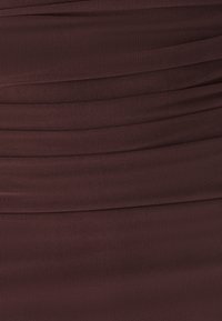Gros plan sur un tissu brun foncé avec des plis horizontaux et une texture en maille fine.