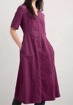 Robe en coton violet avec des manches courtes, un devant à boutons et deux poches latérales ; longueur au genou avec une texture lisse et une coupe décontractée.
