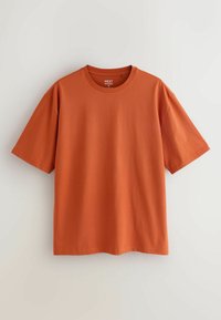 T-shirt à manches courtes col rond couleur rouille, taille moyenne, suspendu sur un fond neutre clair.