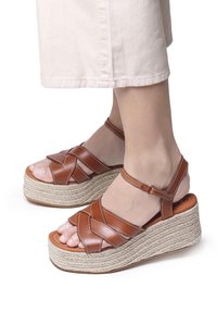 Sandali a zeppa in pelle marrone con cinturini incrociati, platfond in juta intrecciata e dettagli con cinturino alla caviglia. Design open-toe con accenti testurizzati.