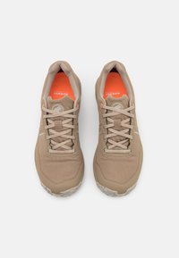 Beige Sportchuhe mit einem glatten, samtartigen Obermaterial, reflektierenden Akzenten und einer leuchtend orangefarbenen Innensohle. Verfügt über eine Standard-Schnürung und eine robuste Sohle.