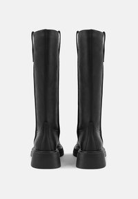 Botas de cuero negro hasta la rodilla con una textura suave, punta redonda y una suela de goma gruesa. Cuentan con tiradores en la parte superior para facilitar su uso.