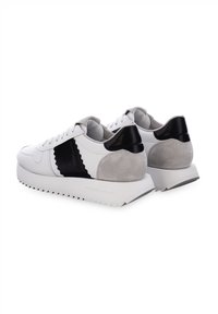 Weiße Leder-Sneaker mit schwarzen und grauen Wildlederakzenten, strukturierten Oberflächen, dicker Sohle mit Zickzackmuster und traditionellem Schnürdesign.