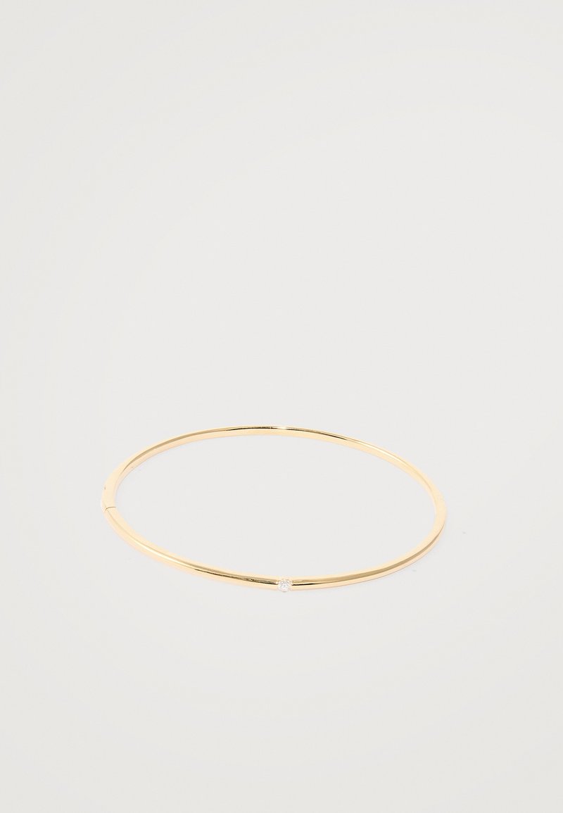 Gold bangle bracelet with a thin, circular design featuring a small, embedded clear gemstone at the front. Smooth, polished finish.