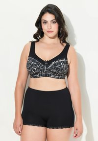 Sujeción en blanco y negro con un patrón, con tirantes anchos y cierre de gancho, combinado con braguitas tipo boyshorts con encaje negro, textura de tela suave.