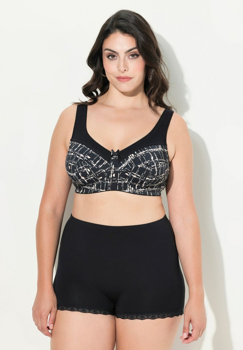 Sujeción en blanco y negro con un patrón, con tirantes anchos y cierre de gancho, combinado con braguitas tipo boyshorts con encaje negro, textura de tela suave.