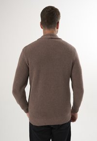 Pruun ribaga kudumiskampsun, millel on krae, pikad varrukad ja tekstuuriline pind, koos mustade pükstega. Tagantvaade näitab kanga detaile.