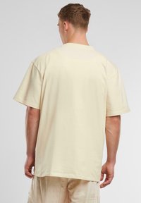 Beige short-sleeve t-shirt made of soft cotton. Boxy fit with a round neckline and seamless shoulders. Plain design with no patterns or graphics.
