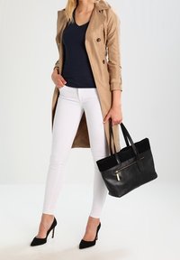 Černá kožená kabelka s kontrastní horní částí, zlatým zipem a pevnými uchy; v kombinaci s béžovým trenčkotem a bílými úzkými džíny.