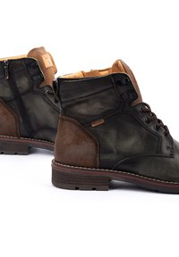 Botas de cuero verde oscuro con acentos marrones, paneles texturizados, cordones y cremalleras. Suela resistente con un ribete contrastante, que ofrece un diseño robusto.