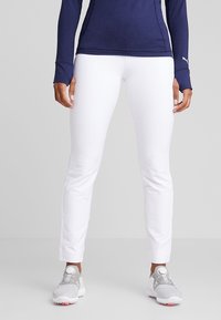 Vita träningsbyxor med slim fit, tillverkade av ett slätt material. Kombineras med grå sneakers med ett unikt snörningssystem.