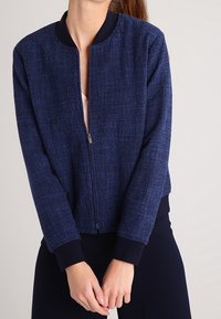Marineblaue Bomberjacke aus strukturiertem Stoff, mit einem Reißverschluss vorne, geripptem Kragen und Bündchen. Lässiger, kürzer geschnittener Stil.