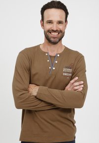 Brun langermet skjorte i et mykt materiale, med rund hals, to-knapps placket og grafisk trykk med røde og blå detaljer.