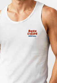 White sleeveless tank top featuring red and blue text: "Pasta La Vista" and "NeverLess®." Smooth fabric with a rounded neckline.
