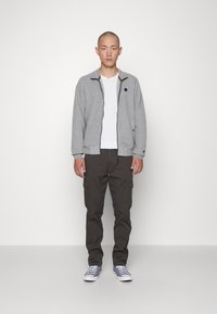 Gray quilted bomber jacket with black zipper and collar detail, white t-shirt, dark cargo pants, and gray sneakers. Simple, functional design.