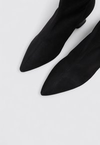 Bottines en velours noir avec un bout pointu et un petit talon. Texture lisse, détails de couture minimalistes et design épuré.